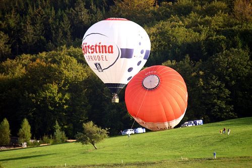 Zwei Heißluftballons beim Aufrüsten auf einer Wiese am Waldrand