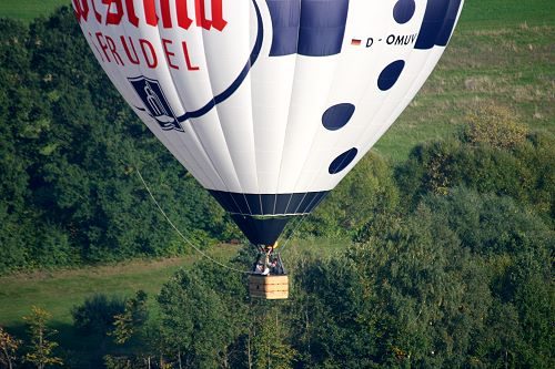 Heißluftballon steigt über einem Waldstück auf