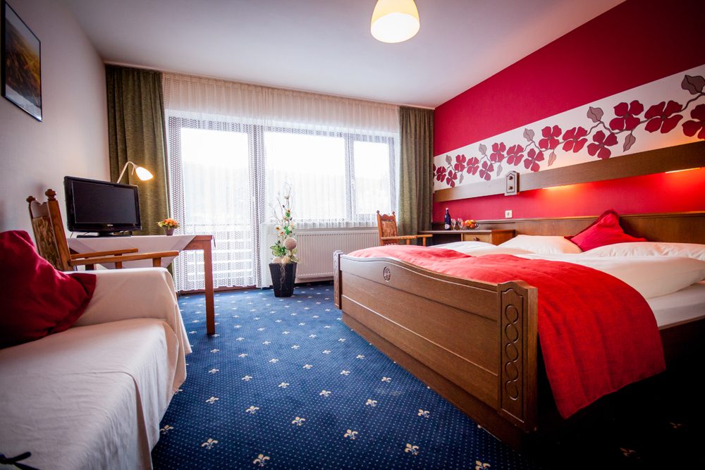 Doppelzimmer mit roter Bettwäsche und blauem Teppich