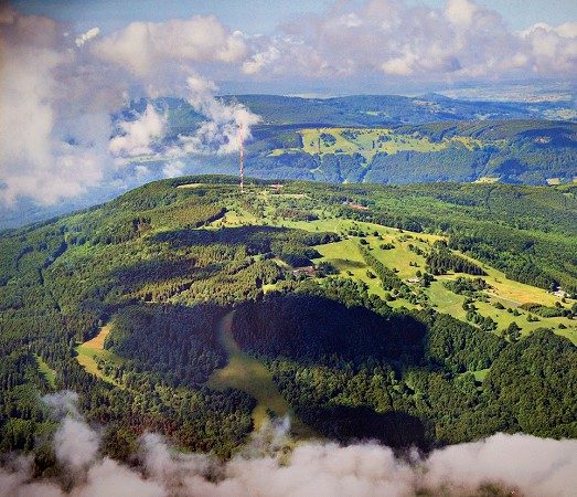 Luftbild der grünen Rhönlandschaft mit dem Kreuzberg über einem Wolkenmeer
