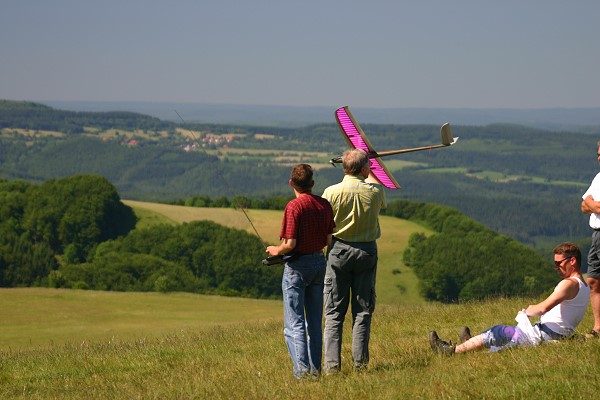 Modellflieger mit einem pinkfarbenen Segelflugmodell auf einer Rhönwiese mit Fernblick