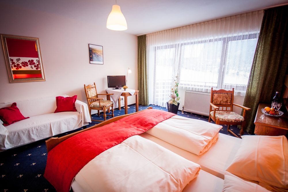 Zimmer mit roter Bettwäsche, Sessel und Blick zum Balkon